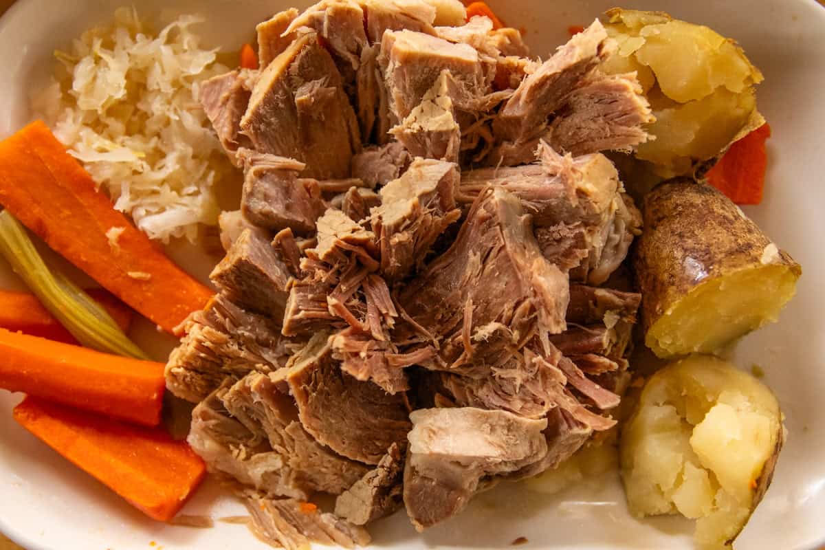 Homemade pork cottage roll with carrots and potatoes on a white serving dish.