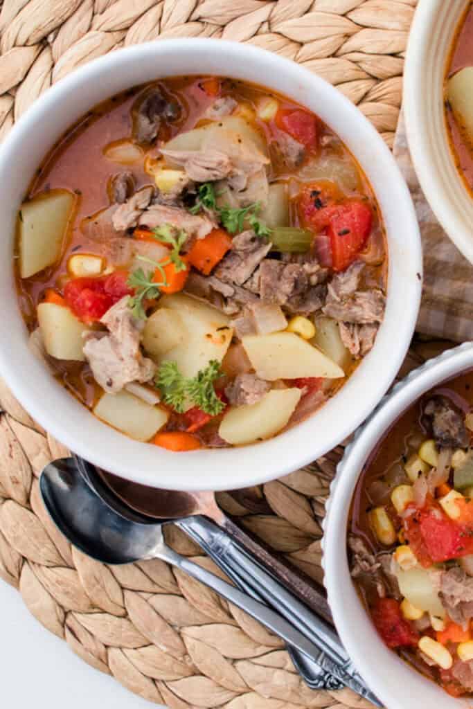 Bowl of steaming hot pork neck bone soup with hearty vegetables on a white table top.