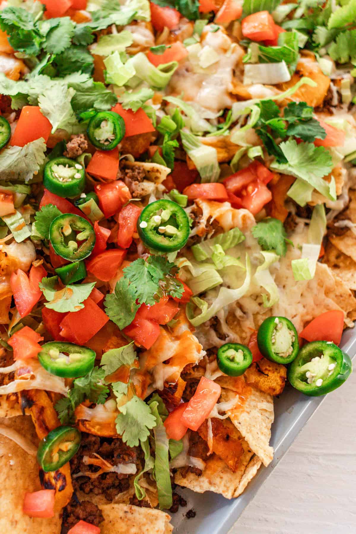 Hearty nachos with a large bed of tortilla chips, topped with ground beef, peppers, onions, roast pumpkin, and garnished with jalapeños, lettuce and tomatoes.