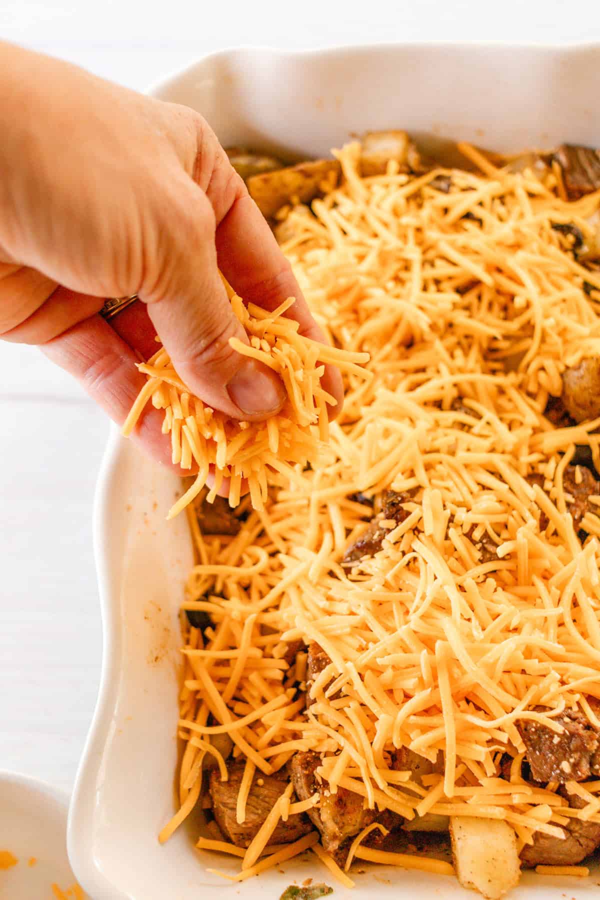 Sprinkling the top of the potatoes and steak with shredded cheddar cheese. 