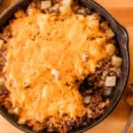 A cast iron skillet full of cheesy venison casserole next to a metal spatula.