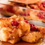 Cranberry french toast casserole with maple syrup drizzling on top of several pieces.