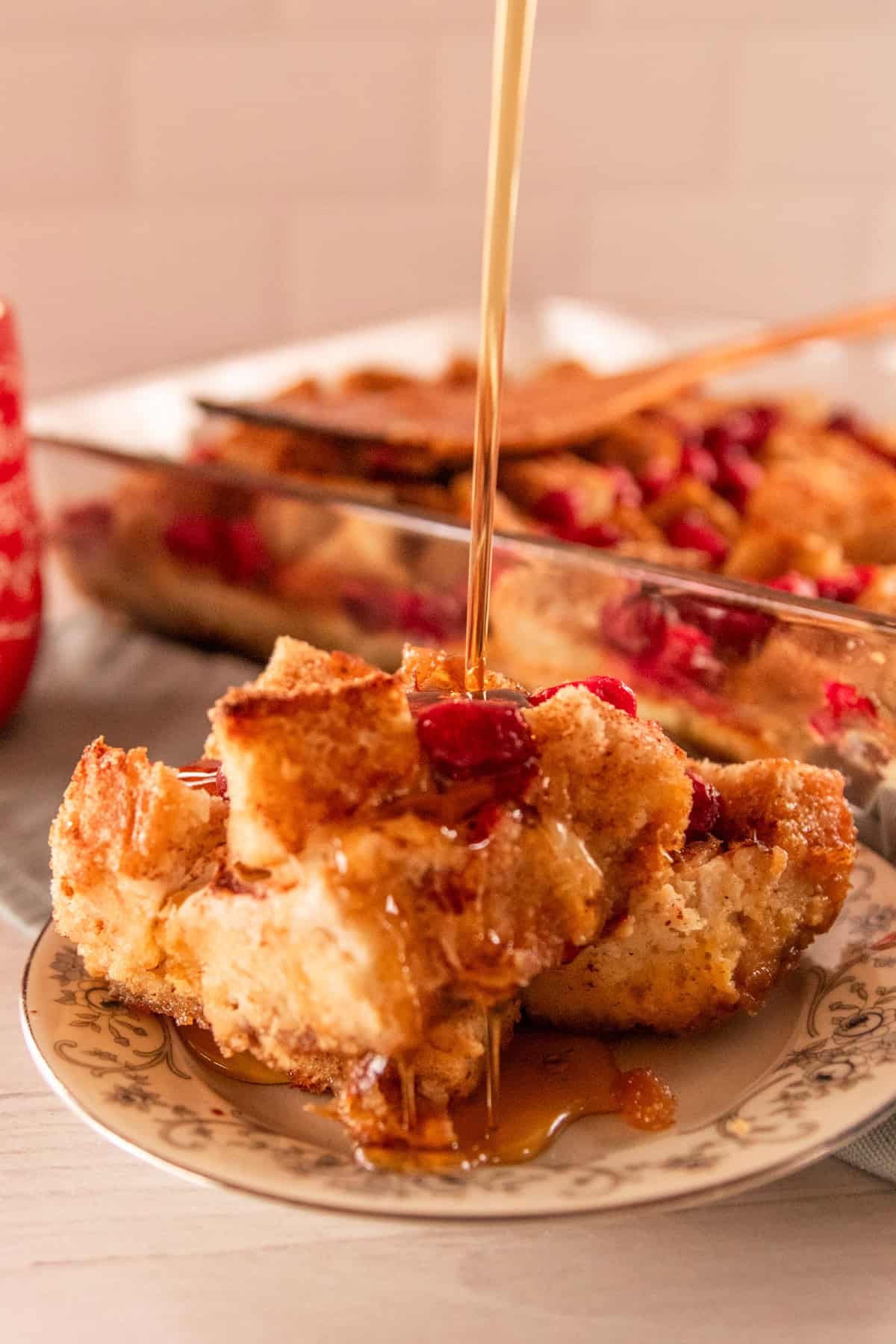 Cranberry french toast pieces stacked on top of a serving plate with the baking dish of extra casserole behind it.