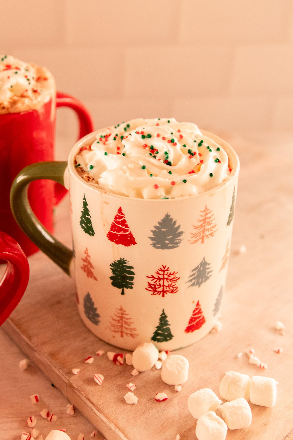 Christmas tree mug with hot chocolate and whipped cream along with a few sprinkles and marshmallows. 