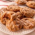 Iced ginger cookies on a white plate with candy cane tablecloth and more cookies cooling in the background.