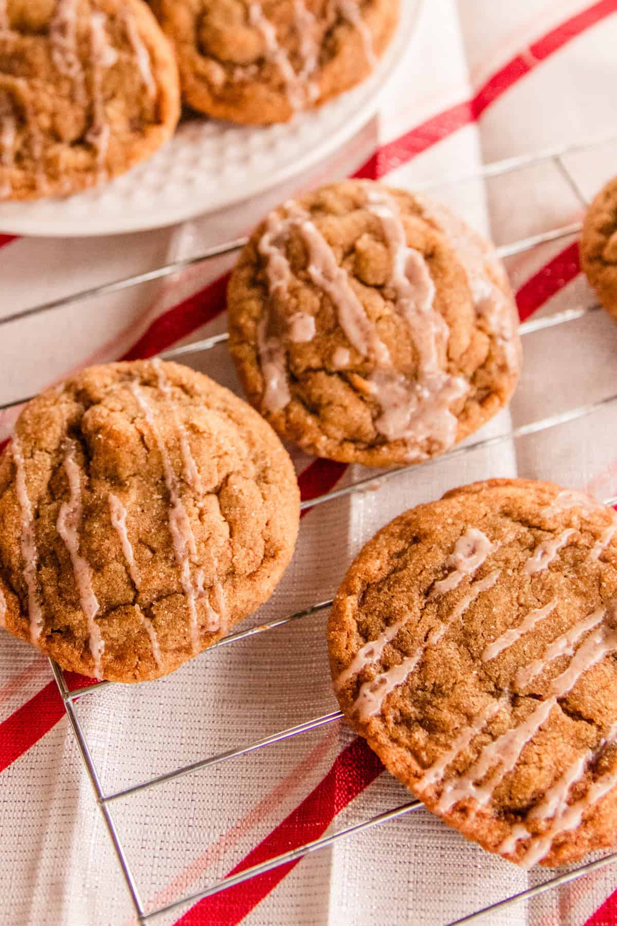 3 ginger cookies cooling on a wire rack with a candy cane tablecloth underneath them. 