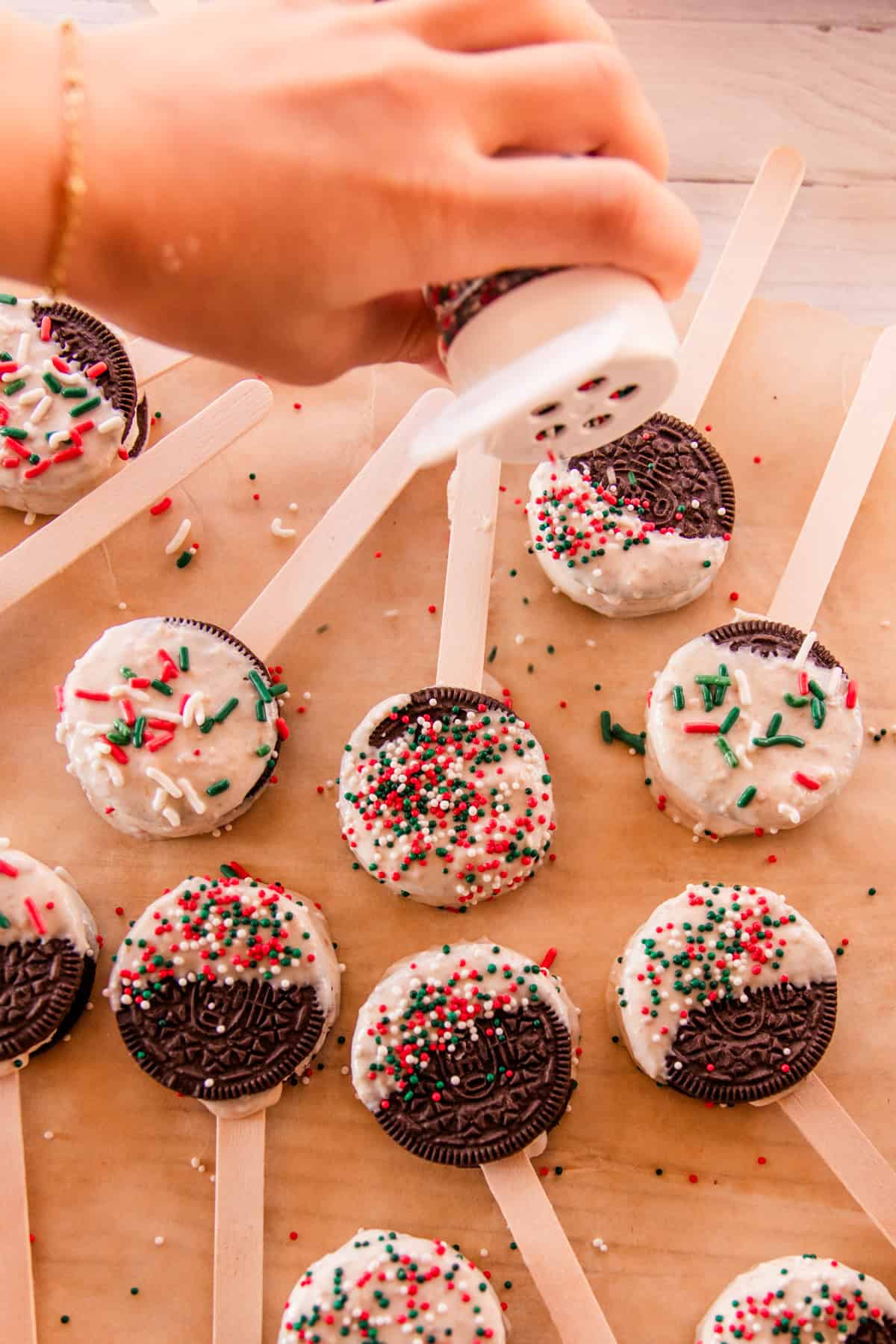 Adding sprinkles to the top of dipped Oreos.