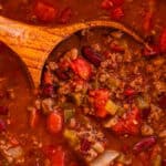 A wooden serving spoon scooping up chili out of the dutch oven.