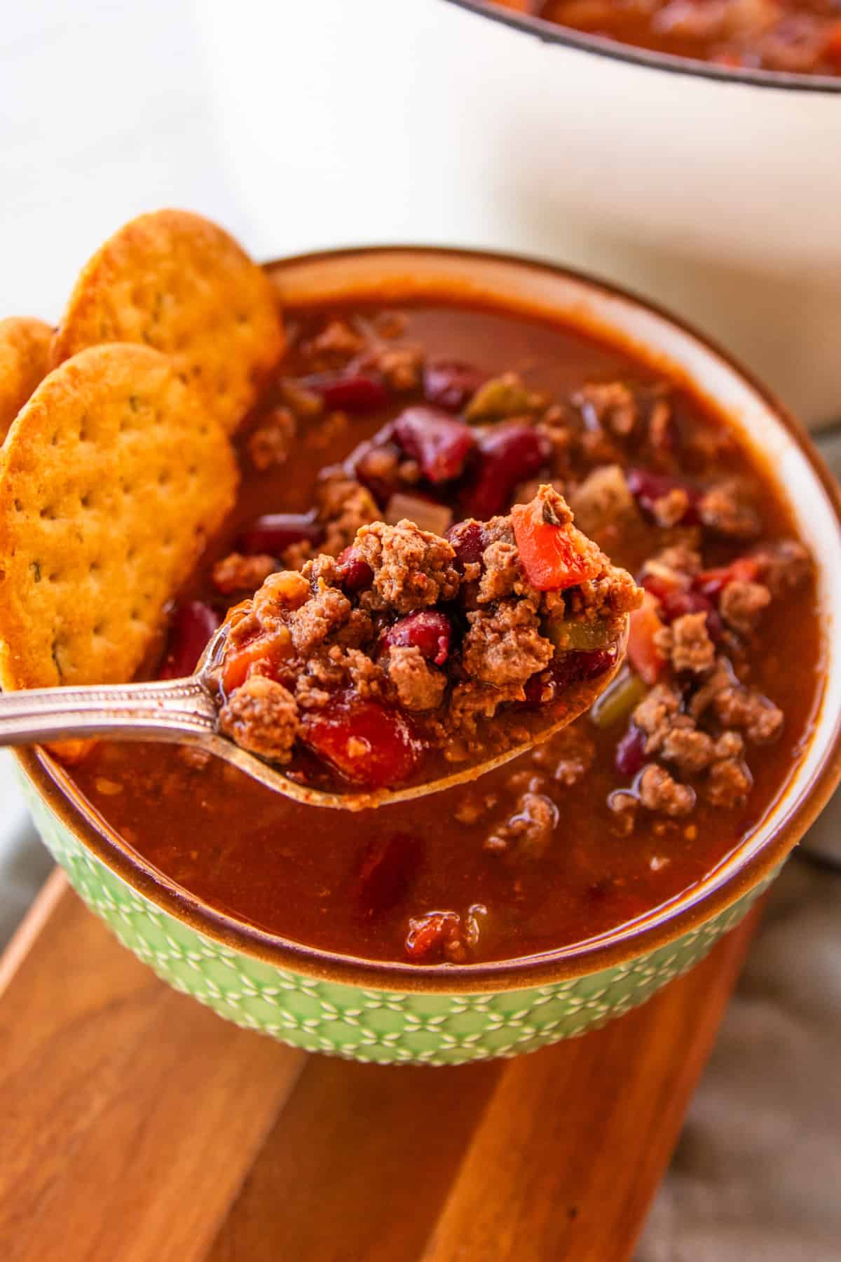 Venison chili in a green bowl with crackers set in next to the side of the bowl.