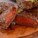 A large venison backstrap cut into several pieces set on a wooden cutting board with green onions on top.