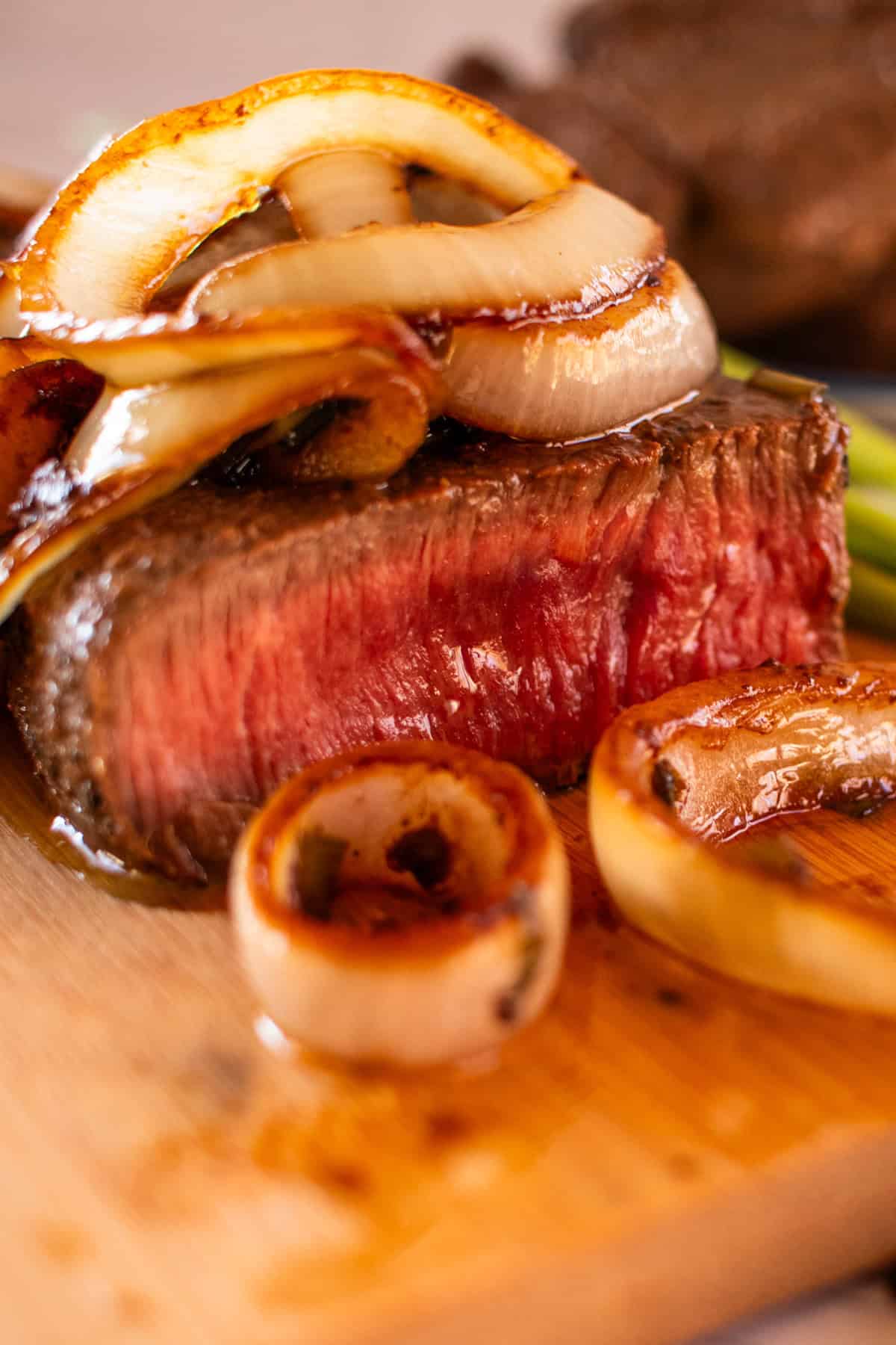 Venison steak sliced on a light colored wooden cutting board and topped with sauteed onions.