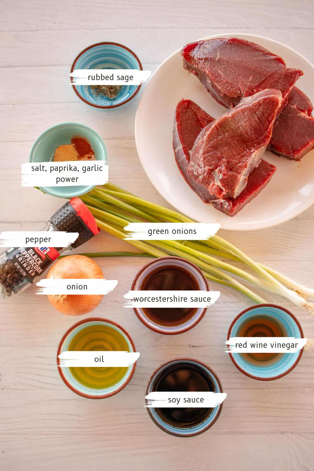 Ingredients for a venison steak recipe on a white wooden table. 