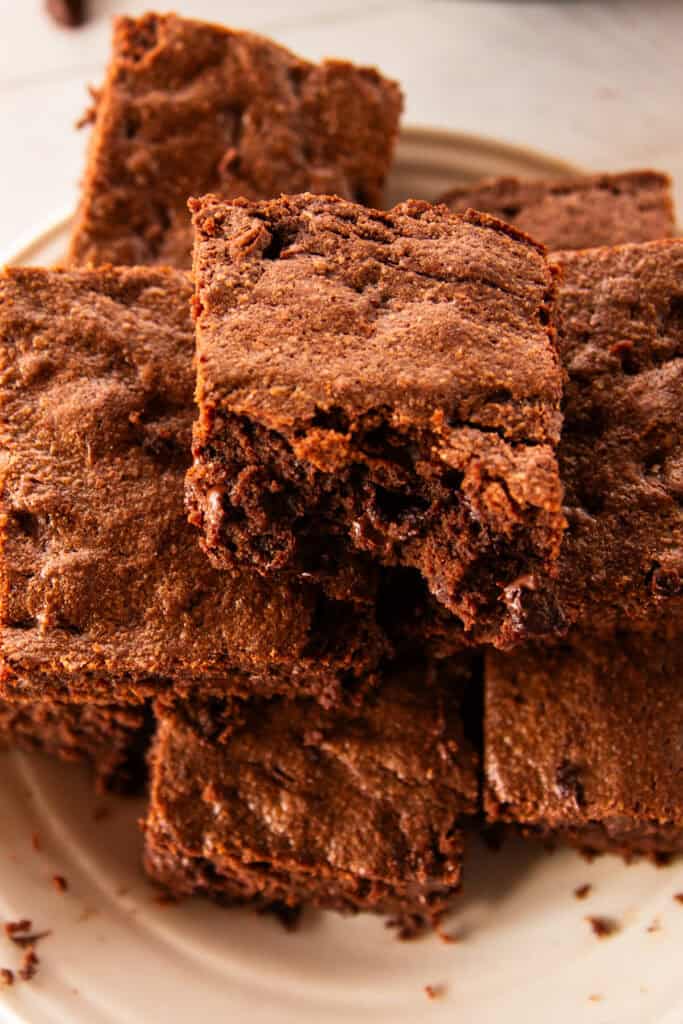A stack of homemade skillet brownies, cut into pieces and stacked on top of each other on a white plate.