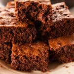 A stack of homemade skillet brownies, cut into pieces and stacked on top of each other on a white plate.