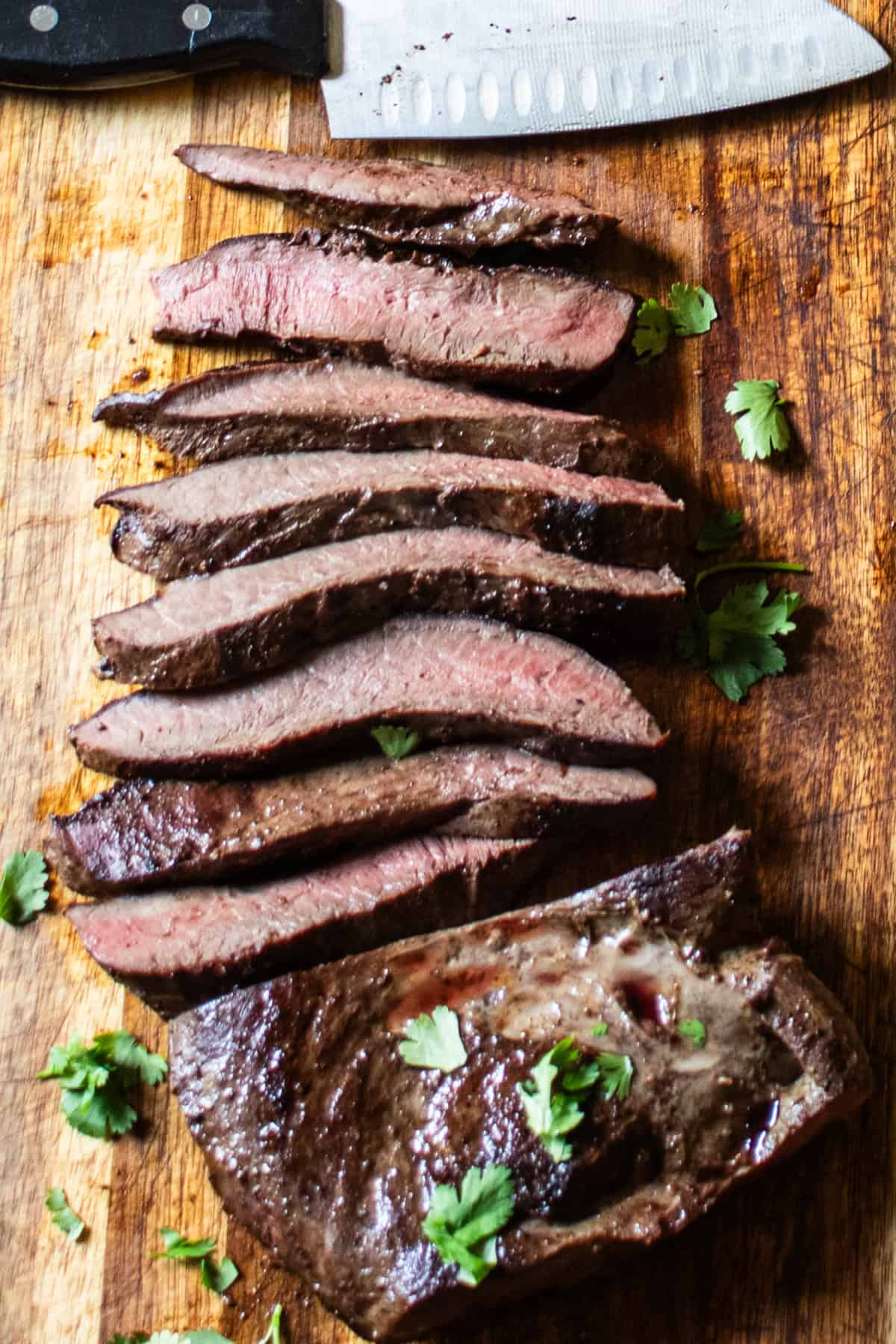 Thinly sliced beef heart on a wooden cutting board with a sharp knife next to it.