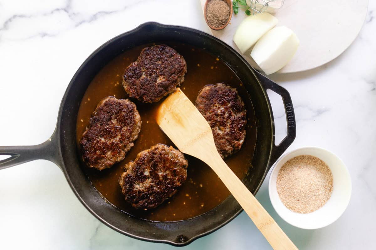 Using a wooden spatula to place the patties into the skillet on top of the gravy. 