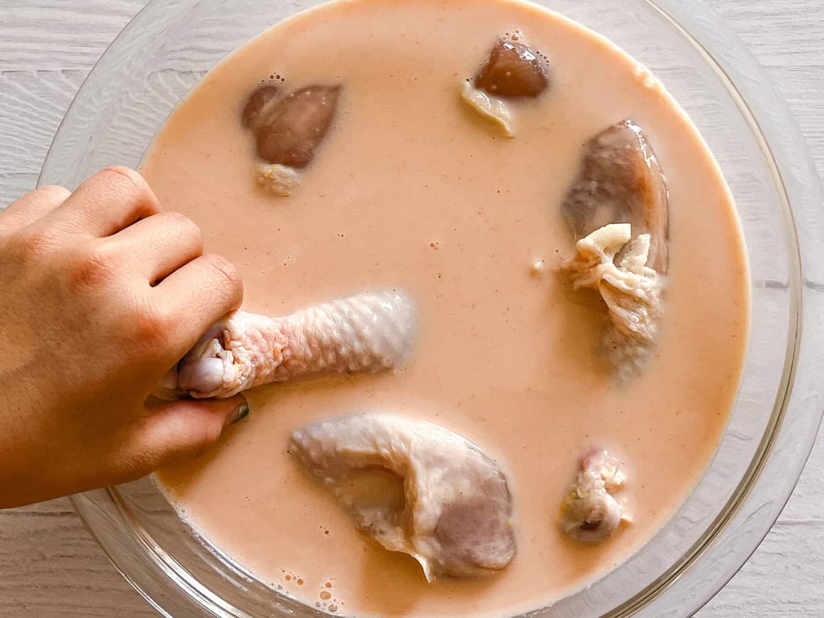 Raw chicken drumsticks being placed in a buttermilk and hot sauce mixture.