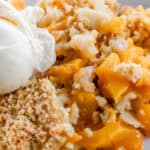 Fresh cast iron peach cobbler served with a scoop of vanilla ice cream on a white plate.