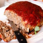 Dutch oven meatloaf with a tangy glaze and several slices cut out of it laying on their side on a white plate.