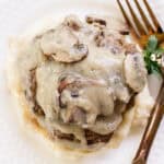 Smothered hamburger steak served on a white plate with gold utensils.