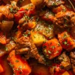 Venison goulash in a white bowl, sprinkled with parsley.