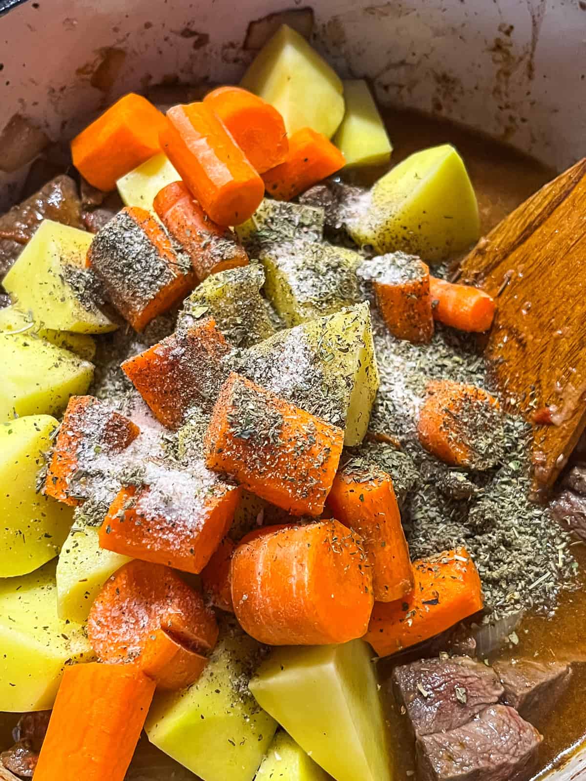 Potatoes and carrots with spices on top of venison and onions in a dutch oven.