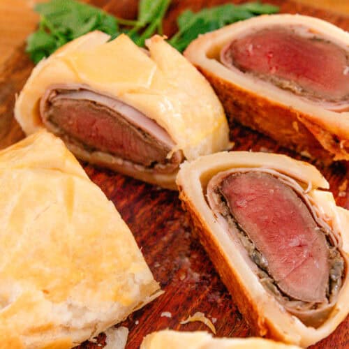 Venison wellington with fresh parsley around it, being served on a wooden table.