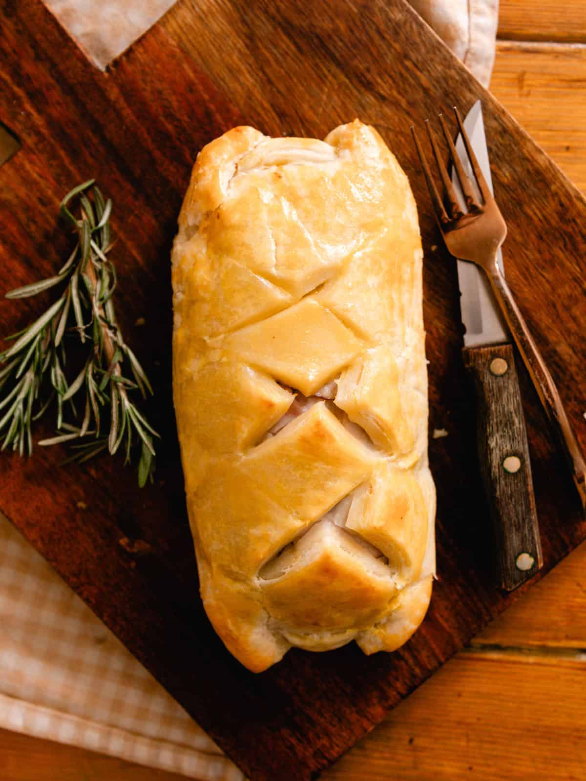 Allowing the venison wellington to rest on a wooden cutting board.