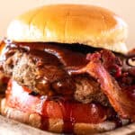 Elk burger with BBQ sauce, bacon, and tomato on a bun.
