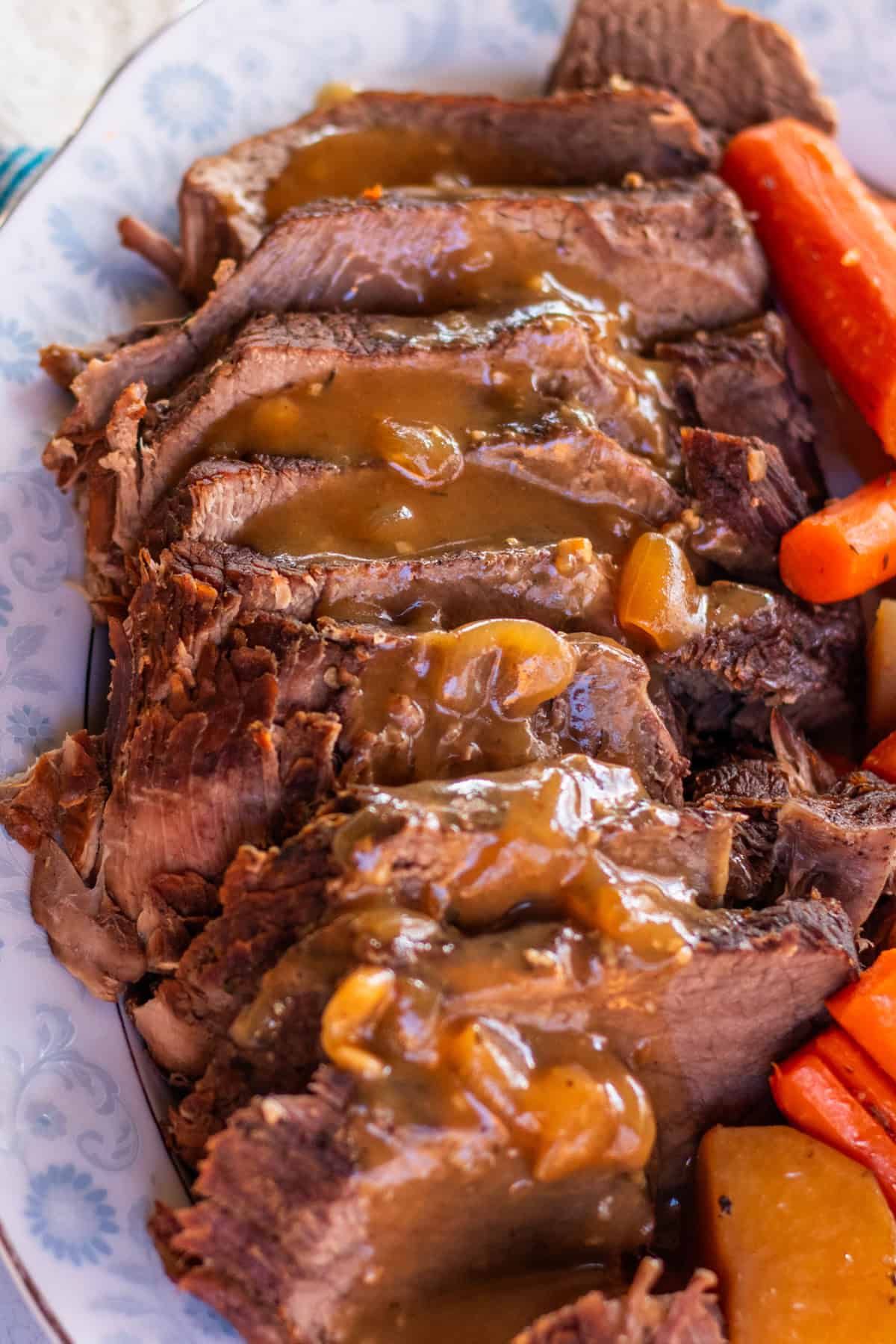 Slices of roast with gravy on a decorative white and blue plate.