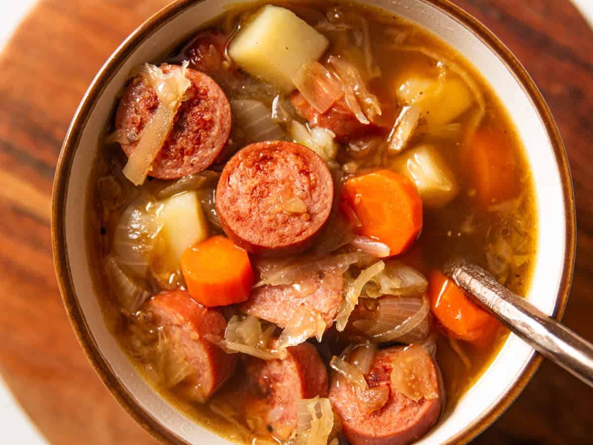 Large chunks of polish sausage, potatoes and carrots with sauerkraut on a small bowl. 