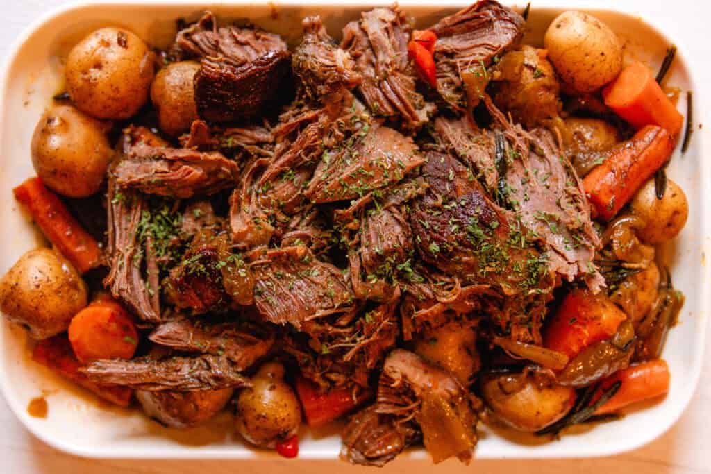 Shredded slow cooker venison roast in a white serving dish.