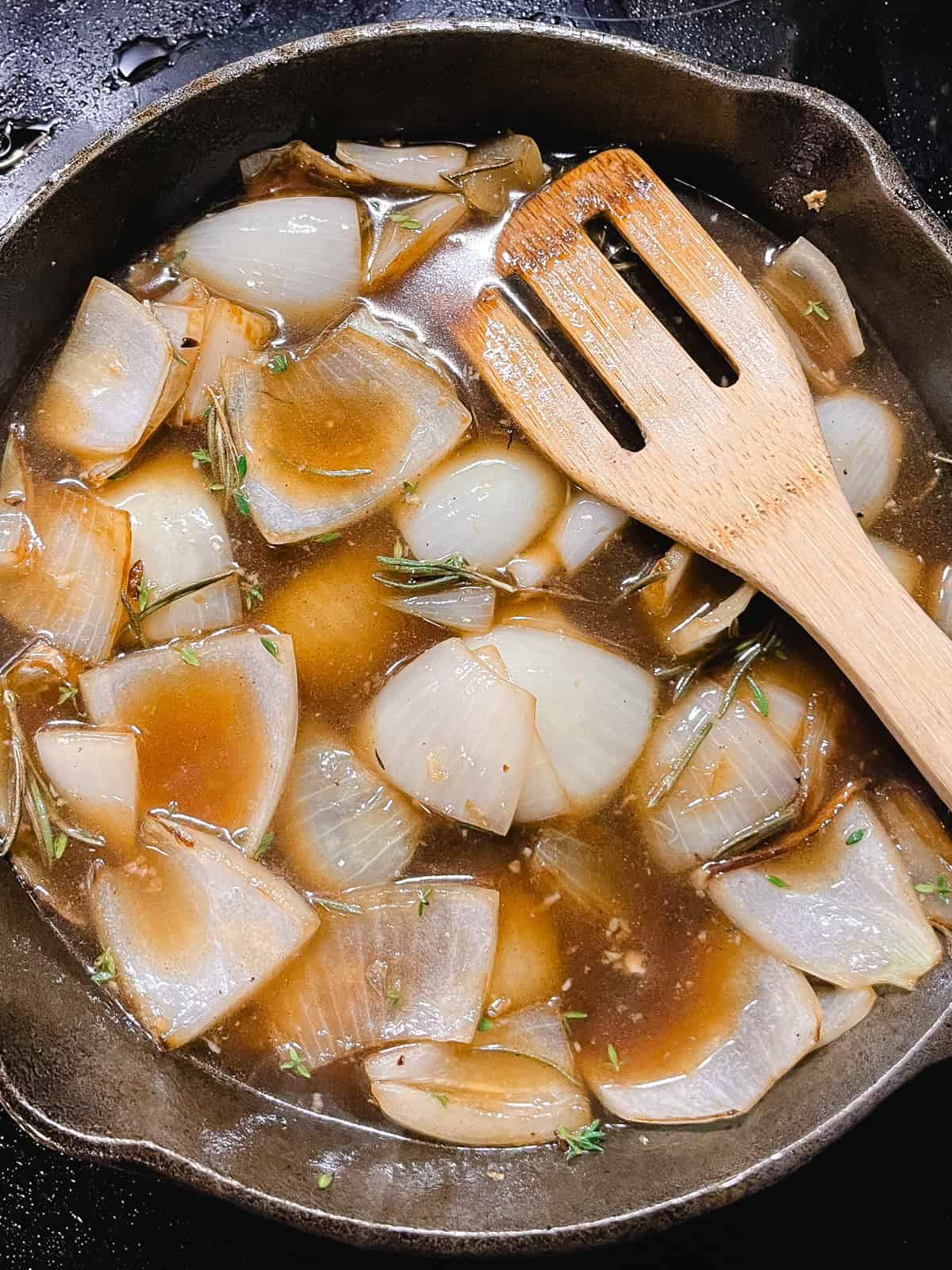 Onions and spices with beef broth in a cast iron skillet.