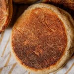 A whole grain english muffin on a striped towel surrounded by other english muffins.