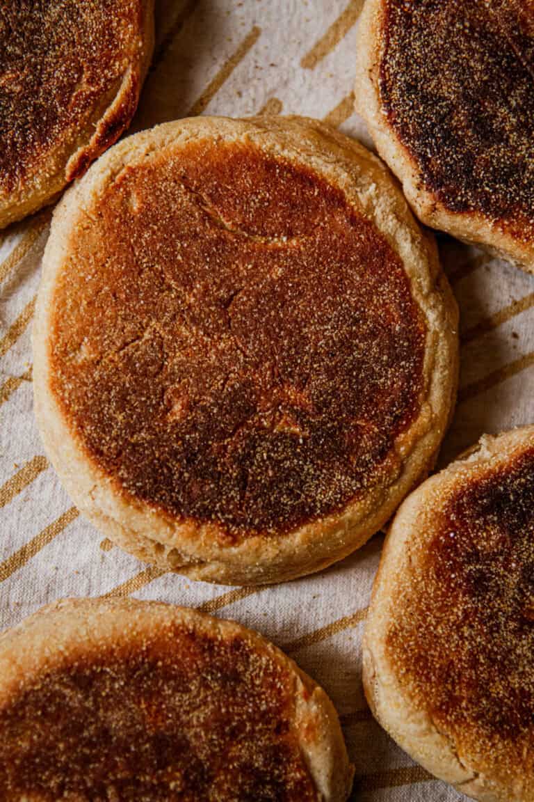 Whole grain English muffins spread out on a striped towel.