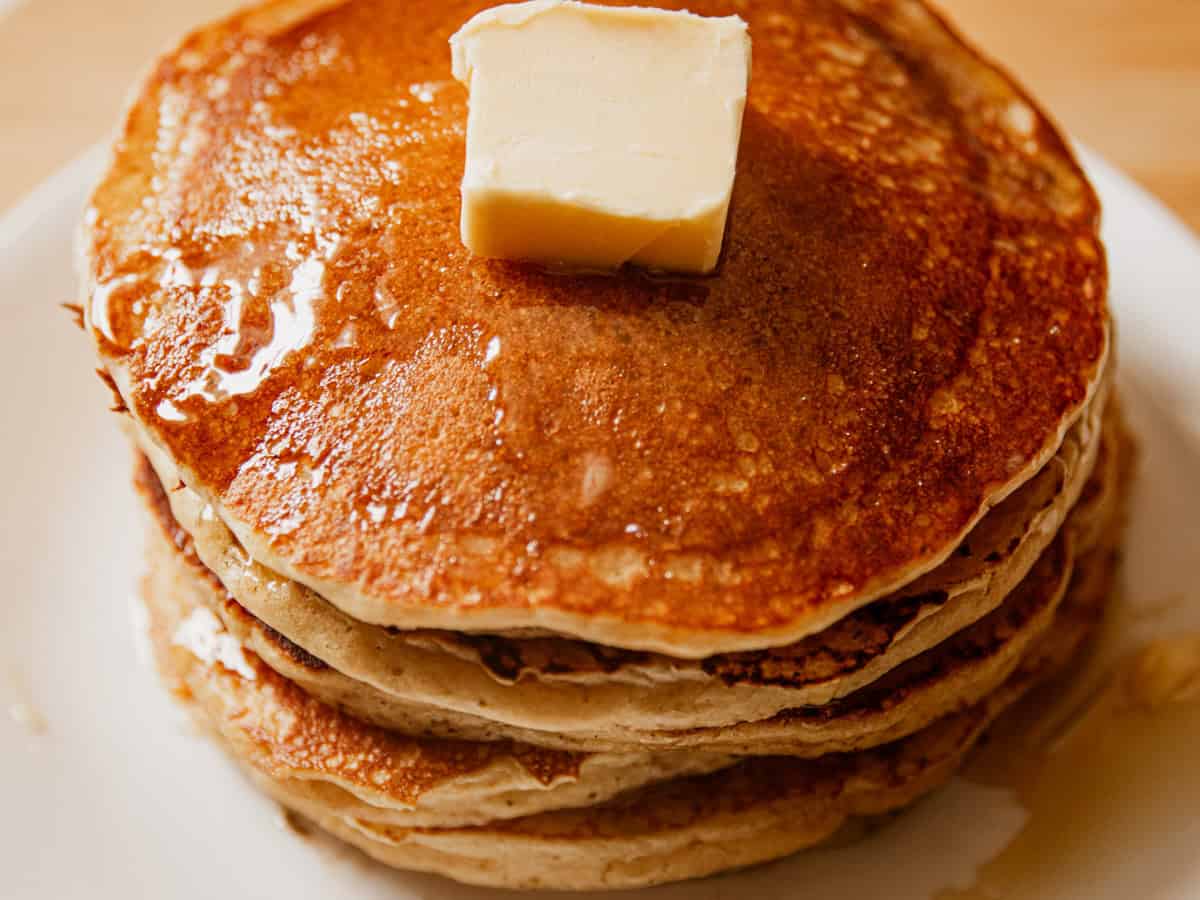 A stack of whole grain pancakes on a white plate with butter and syrup.