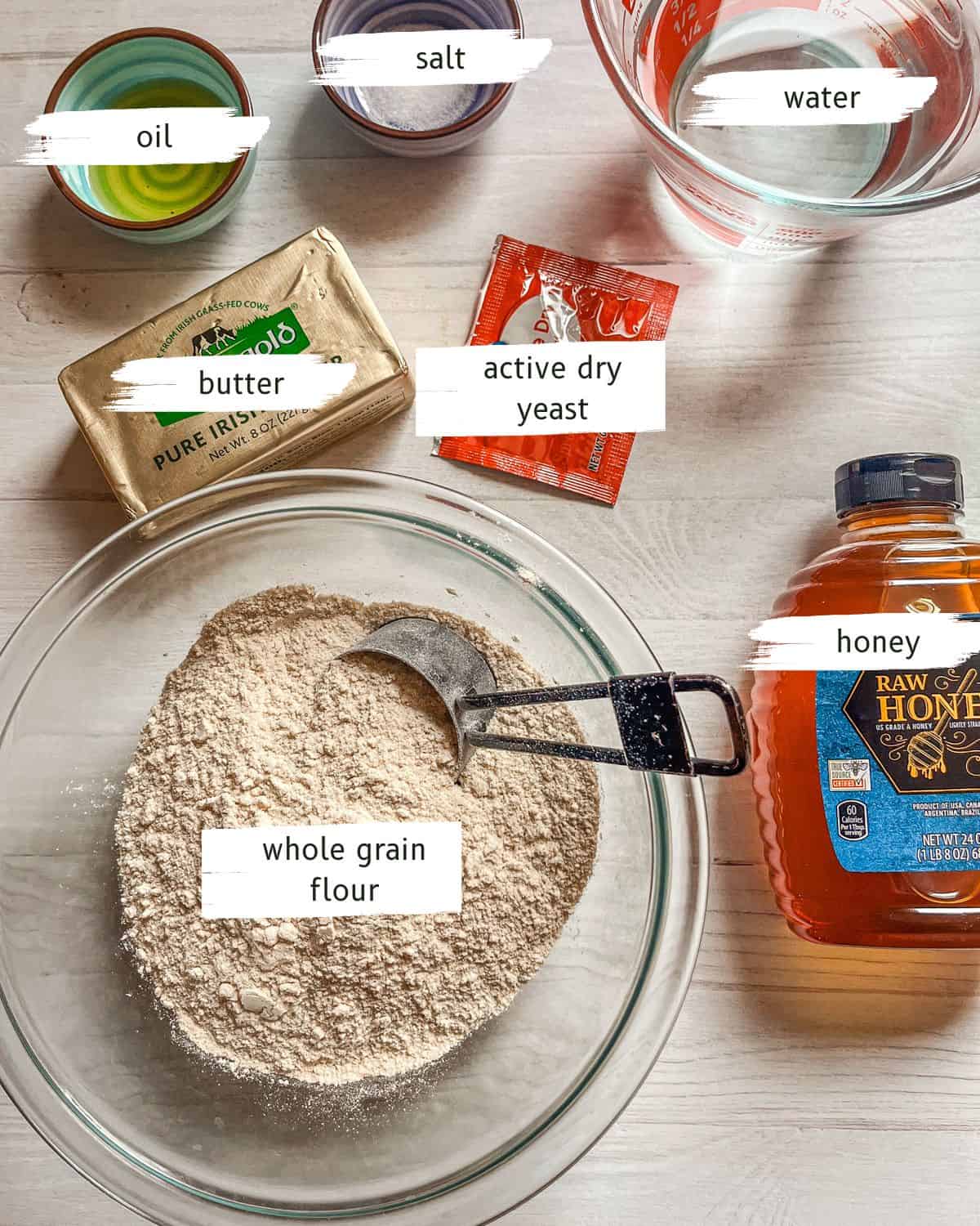 Ingredients for whole grain rolls labeled on a white, wooden table. 