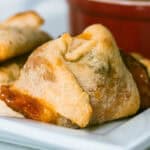 Homemade baked pizza rolls on a white plate with a small red bowl of sauce on the side.