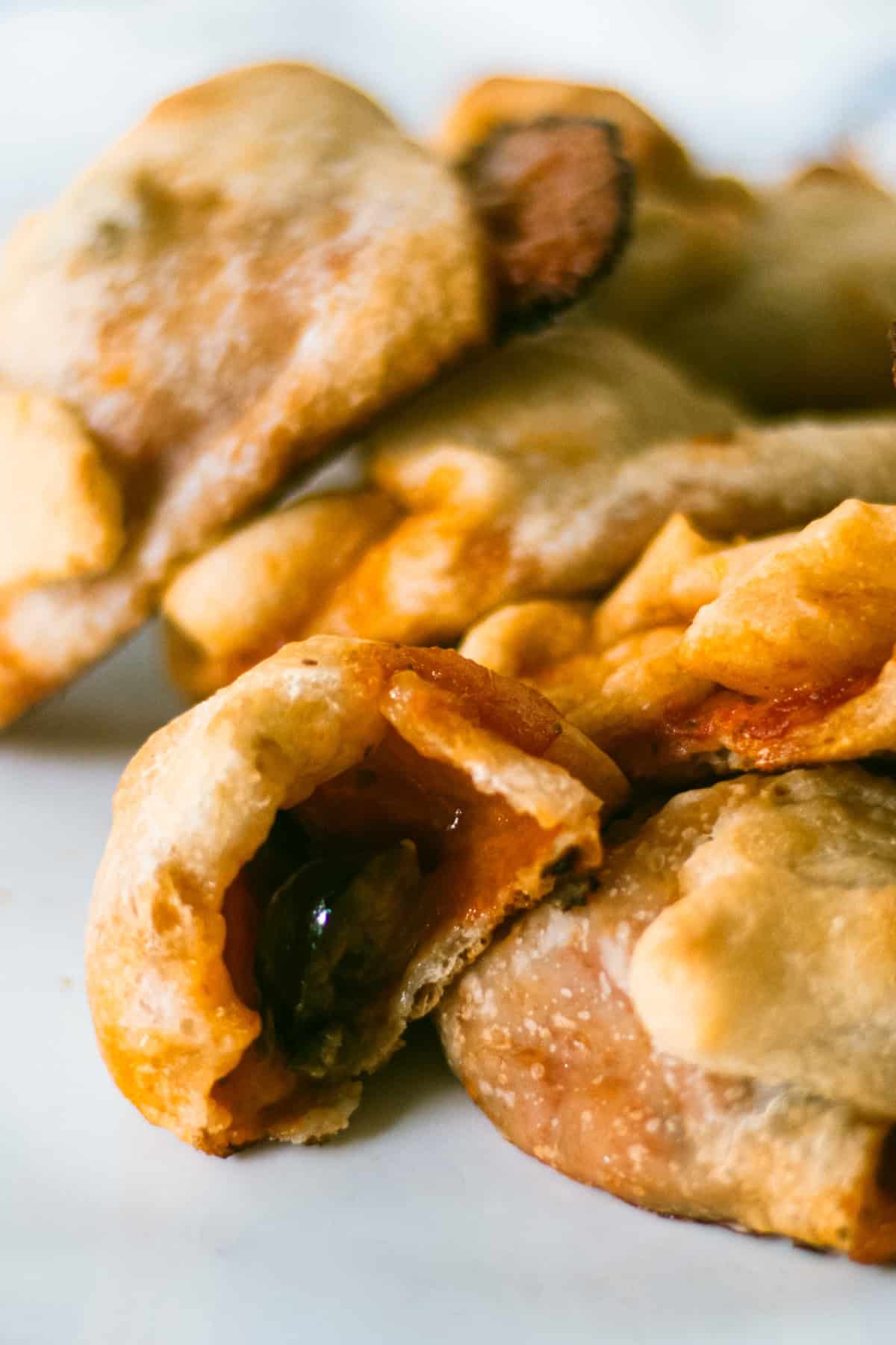 A pile of baked pizza rolls on a white plate, with one cut open to show the filling.