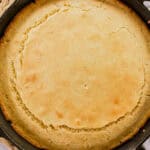 A skillet of cornbread with a puffy middle sitting on a marble table.