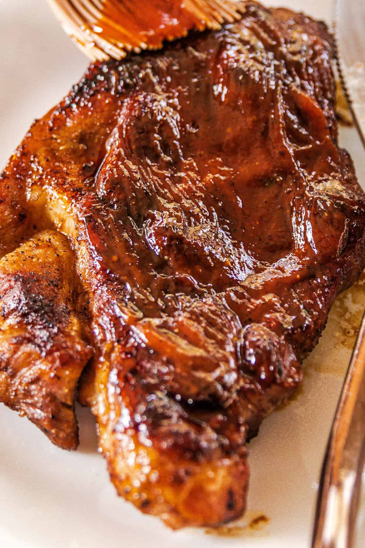 Painting the pork steak with the barbecue sauce while its on a plate.