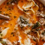 A bowl of sausage tortellini soup with a spoon sticking out of it.