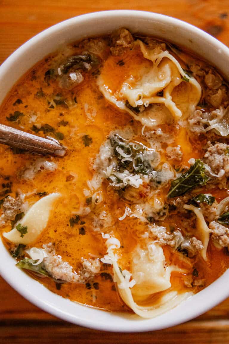 A bowl of sausage tortellini soup with a spoon sticking out of it.