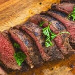 Venison Backstrap sliced on a cutting board with a crispy brown crust and pink in the middle.