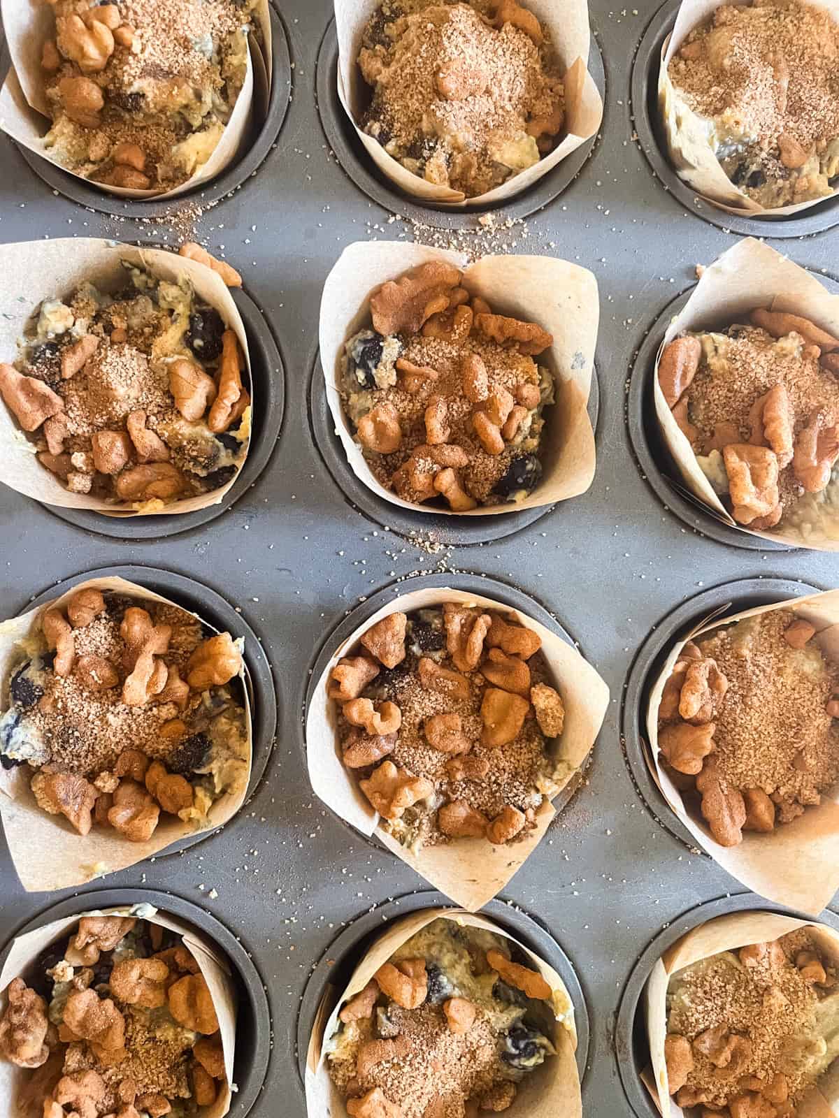 Blueberry muffins in a muffin tin with pecan topping on top of them.