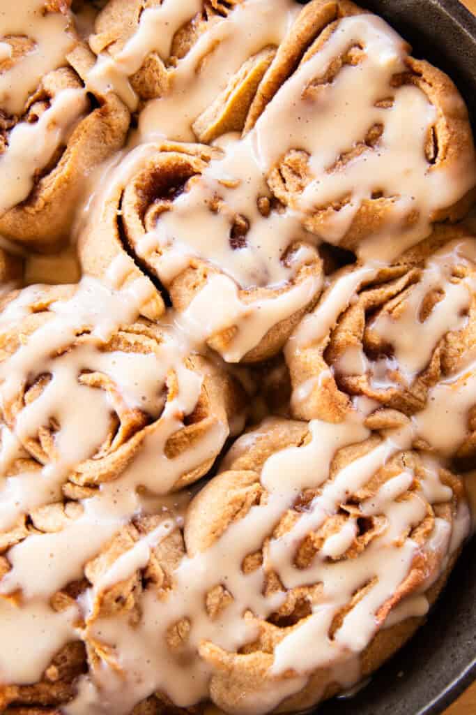 Whole grain cinnamon rolls in a cast iron skillet, drizzled with frosting.