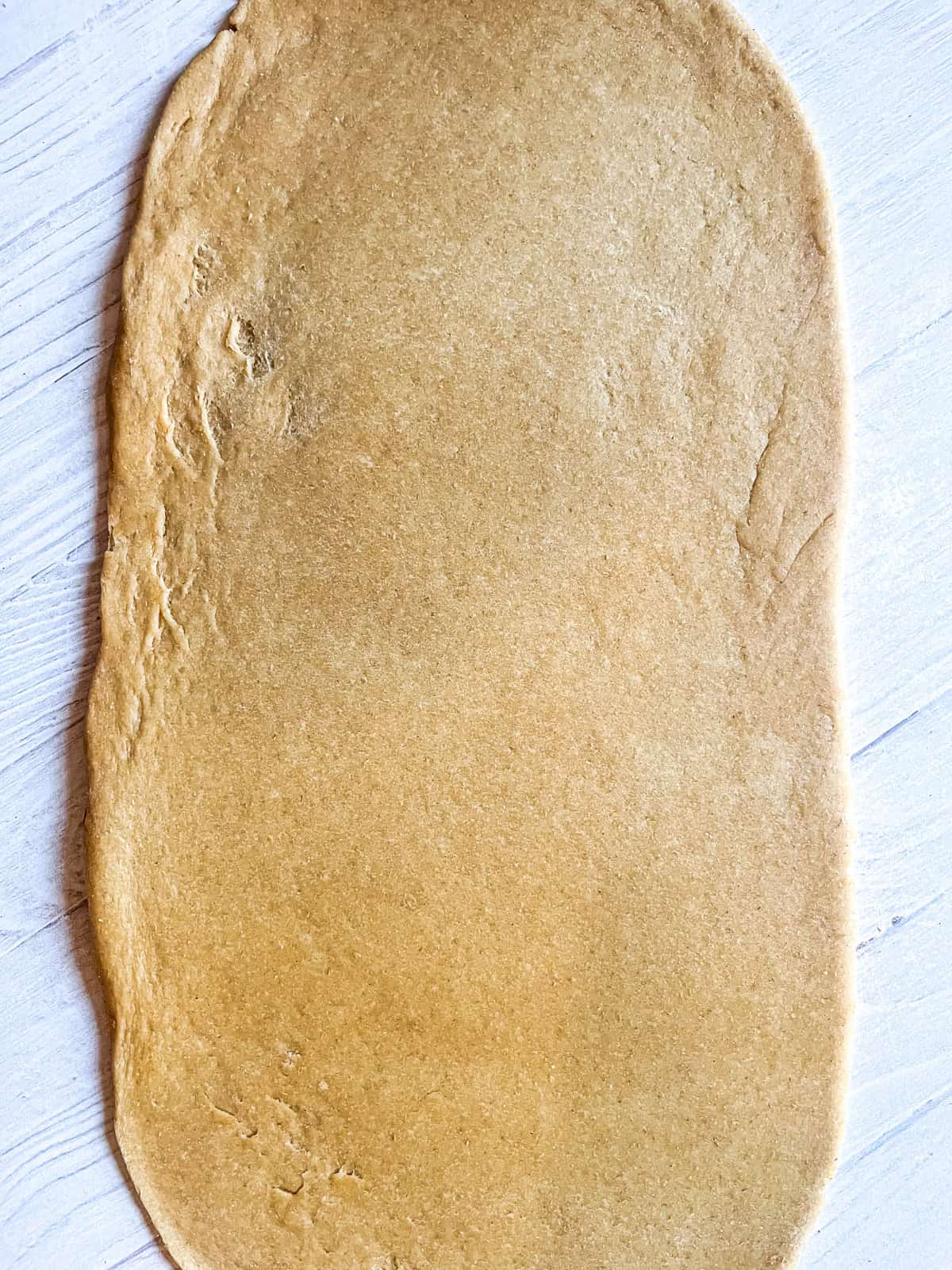 Rolled-out cinnamon roll dough in a rectangle shape.