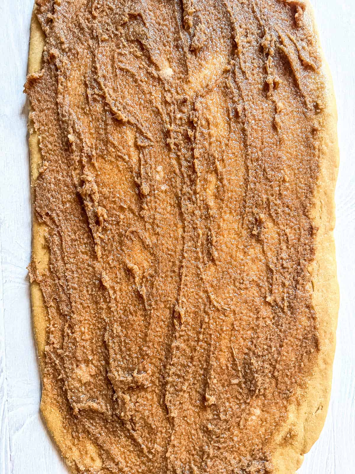 Cinnamon sugar butter spread on rolled-out cinnamon roll dough.