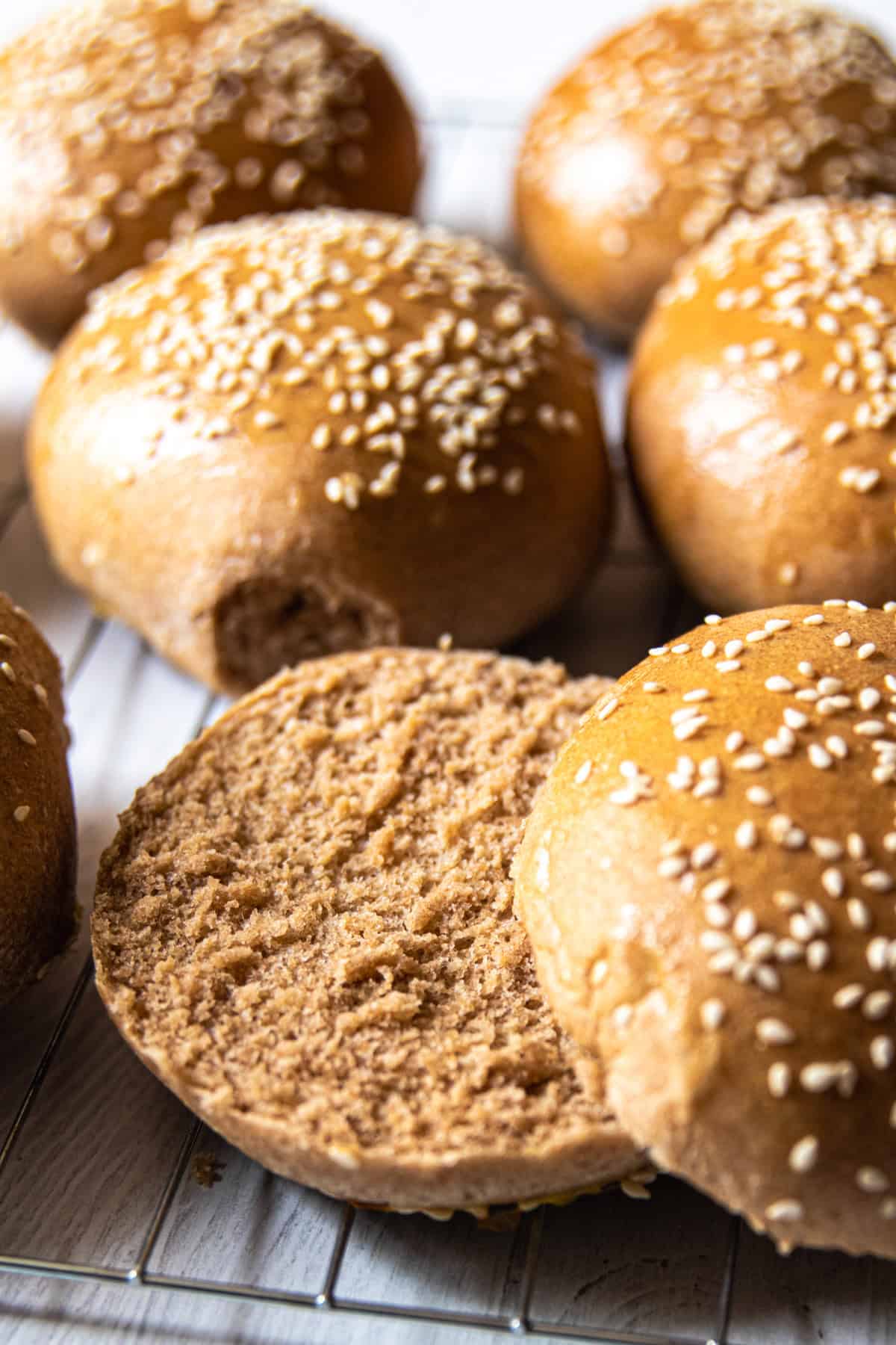 Whole grain buns on a cooling rack, one is sliced in half.