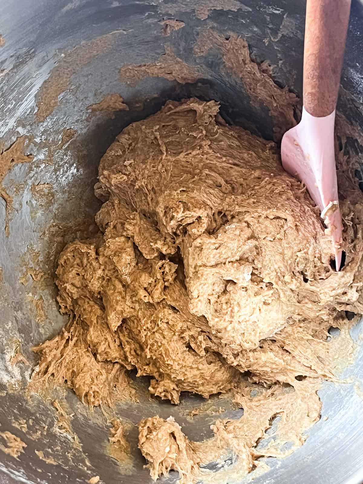 Mixing whole grain bun dough in a metal bowl with a spatula.